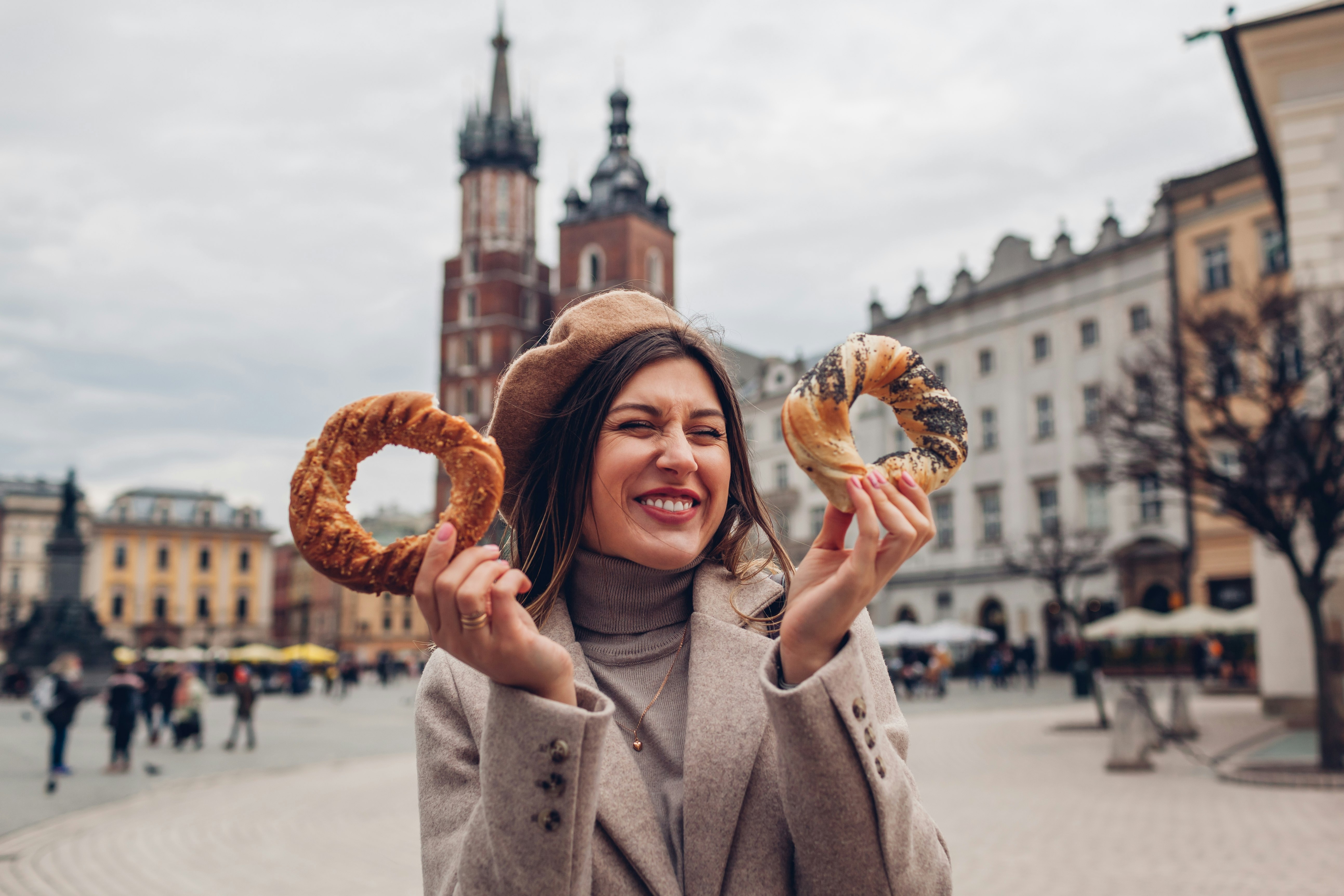 Tourist woman eating bagel obwarzanek traditional polish cuisine snack waling on Market square in Krakow. Traveling Europe in autumn; Shutterstock ID 2057885801; your: Claire Naylor; gl: 65050; netsuite: Online ed; full: Krakow budget