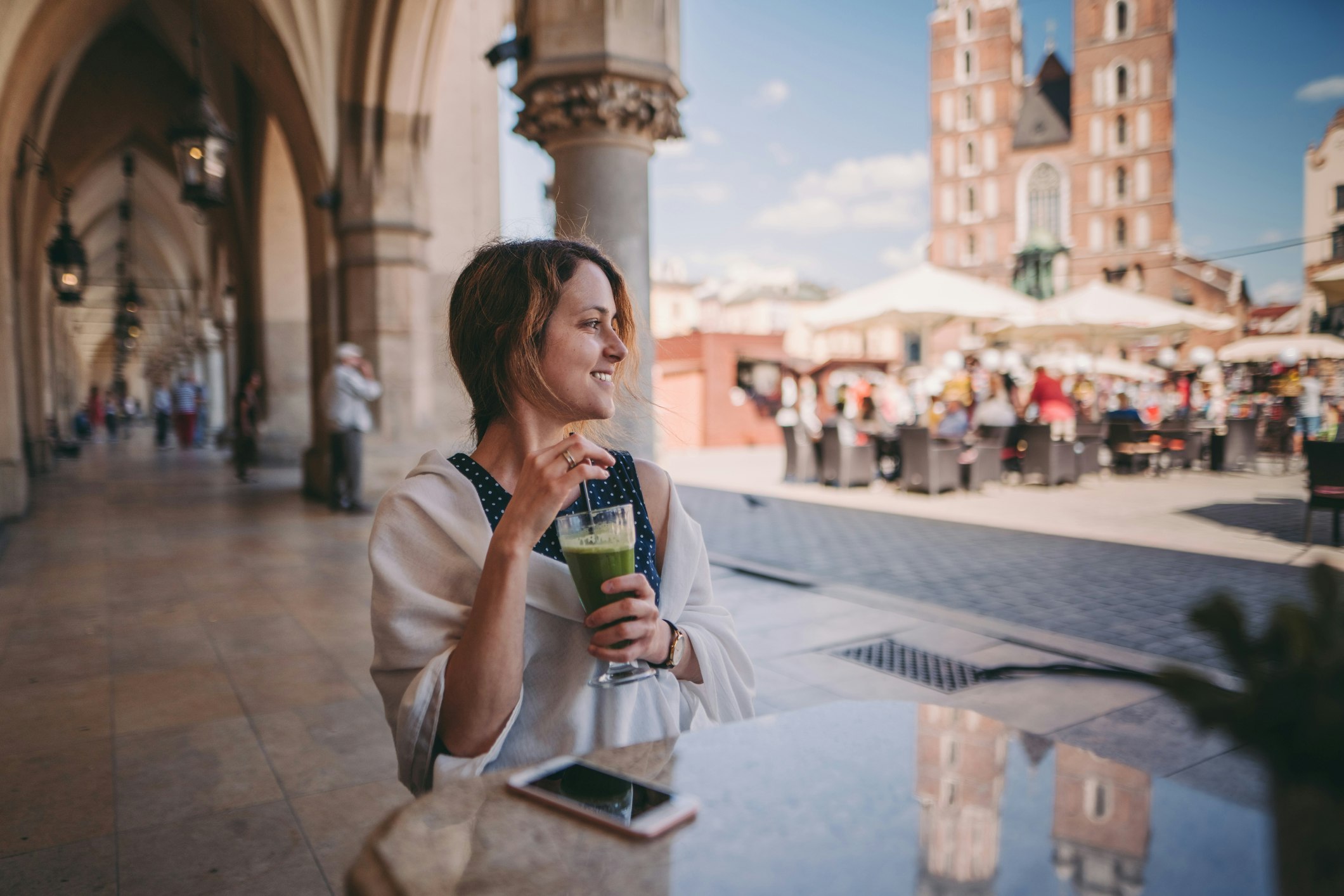 Relaxed woman at cafe drinking green smoothie and enjoying the old town of Krakow