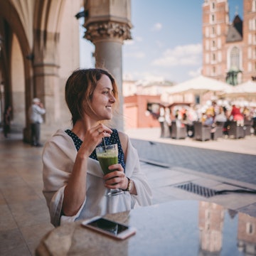 Relaxed woman at cafe drinking green smoothie and enjoying the old town of Krakow