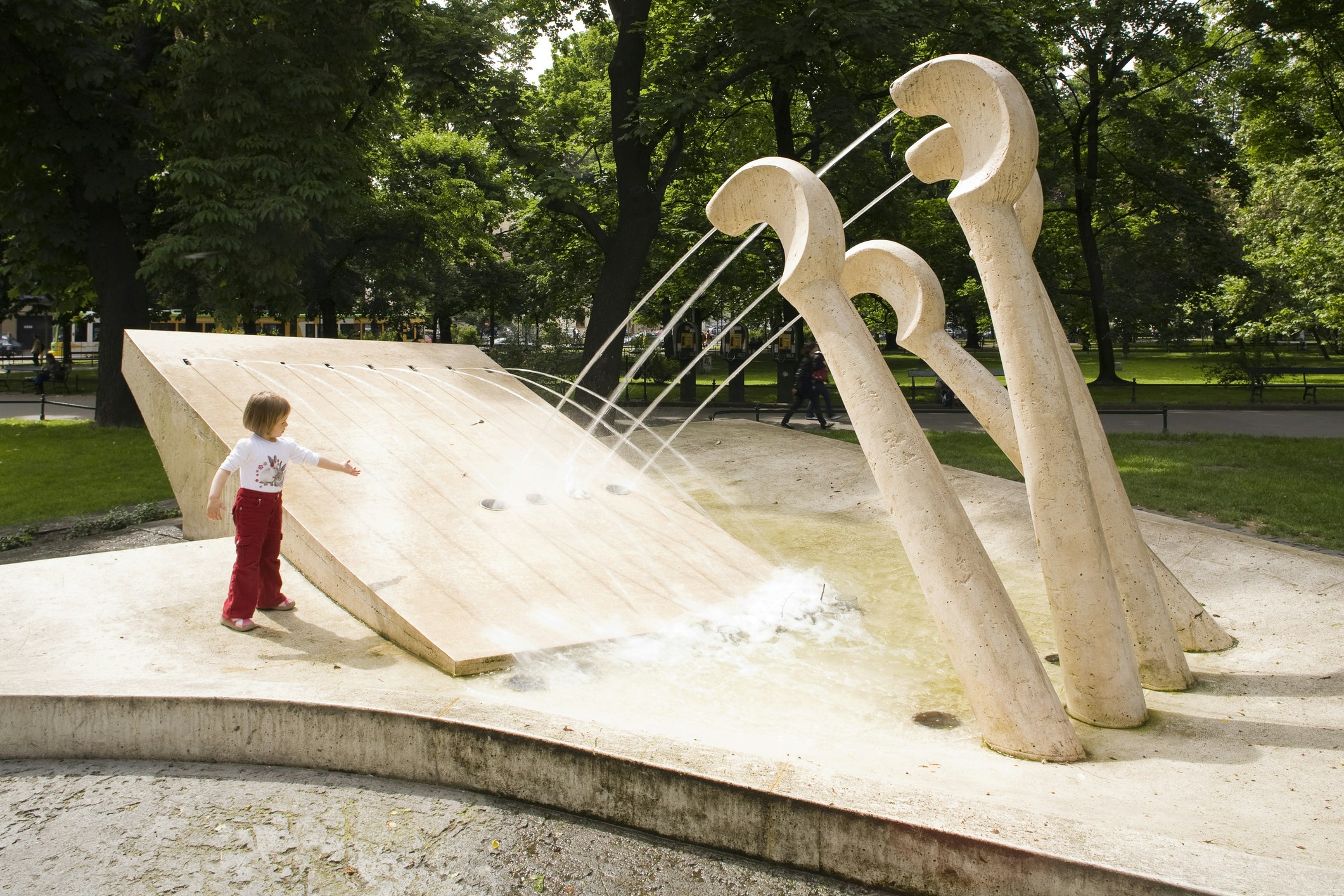 A child plays at a fountain in a park, with jets of water coming from piano keys