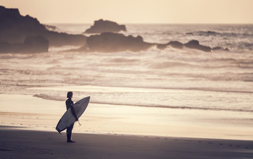 Le surfeur regarde les vagues de Praia do Castelejo en Algarve