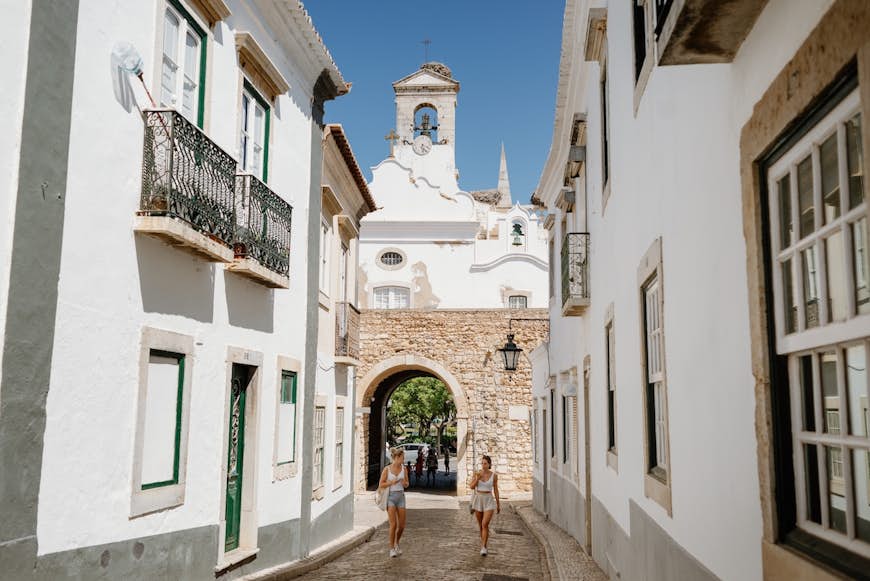 Two young tourist girls walk down a street in the old town of Faro, the Algarve, Portugal