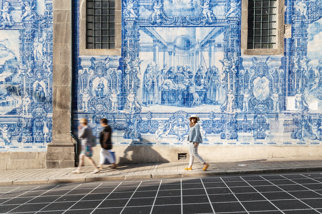 Woman walking in Porto against azulejos wall. Capela das Almas church, Portugal, Europe