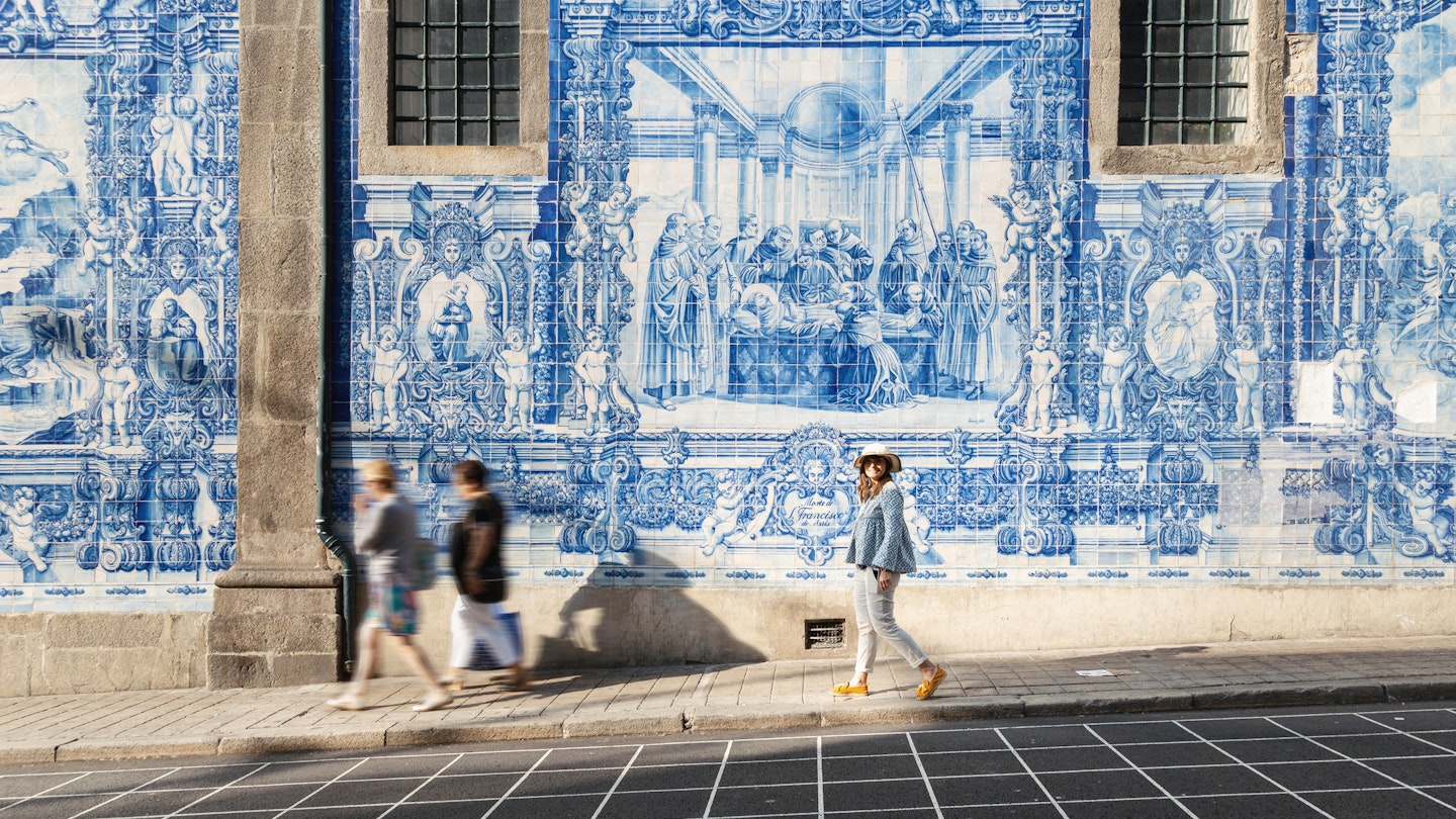 Woman walking in Porto against azulejos wall. Capela das Almas church, Portugal, Europe