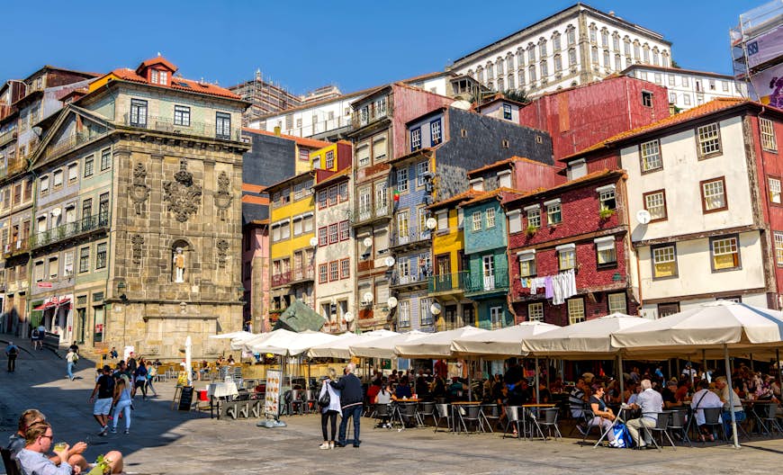 Pedestrians and people seated at tables on the sidewalk in the Ribeira neighborhood against a backdrop of tall, colorful buildings