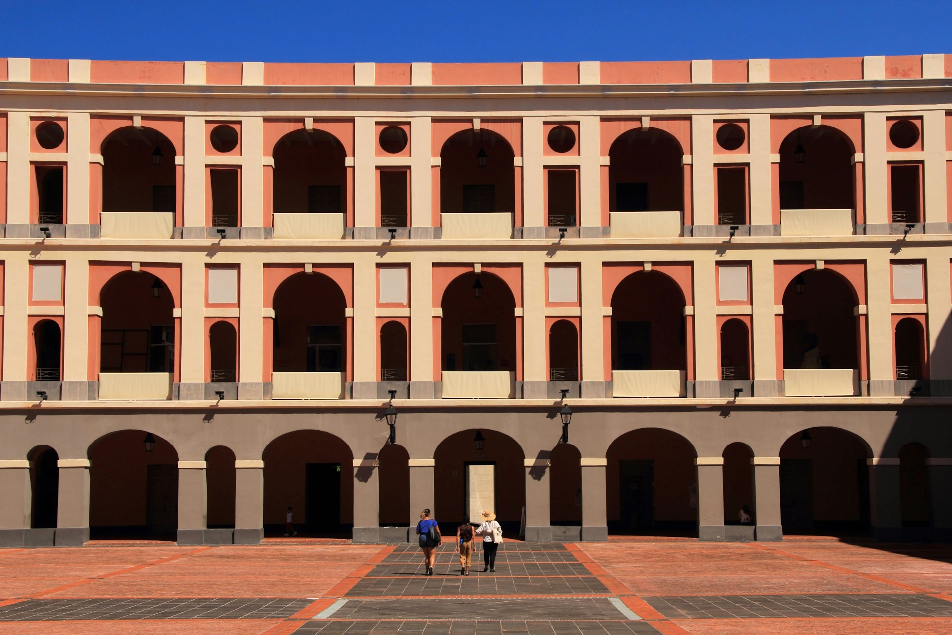 People walking toward the Museo de las Américas in San Juan, Puerto Rico, a towering, three-story facade with rows of arches 