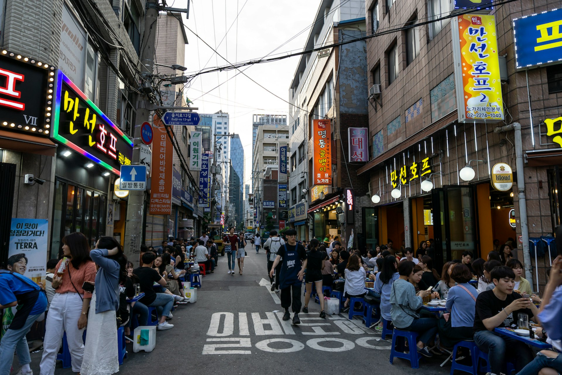 People sit on tables spelling into narrow Nogari Alley, known for traditional bars and dried fish in Euljiro, Seoul, South Korea