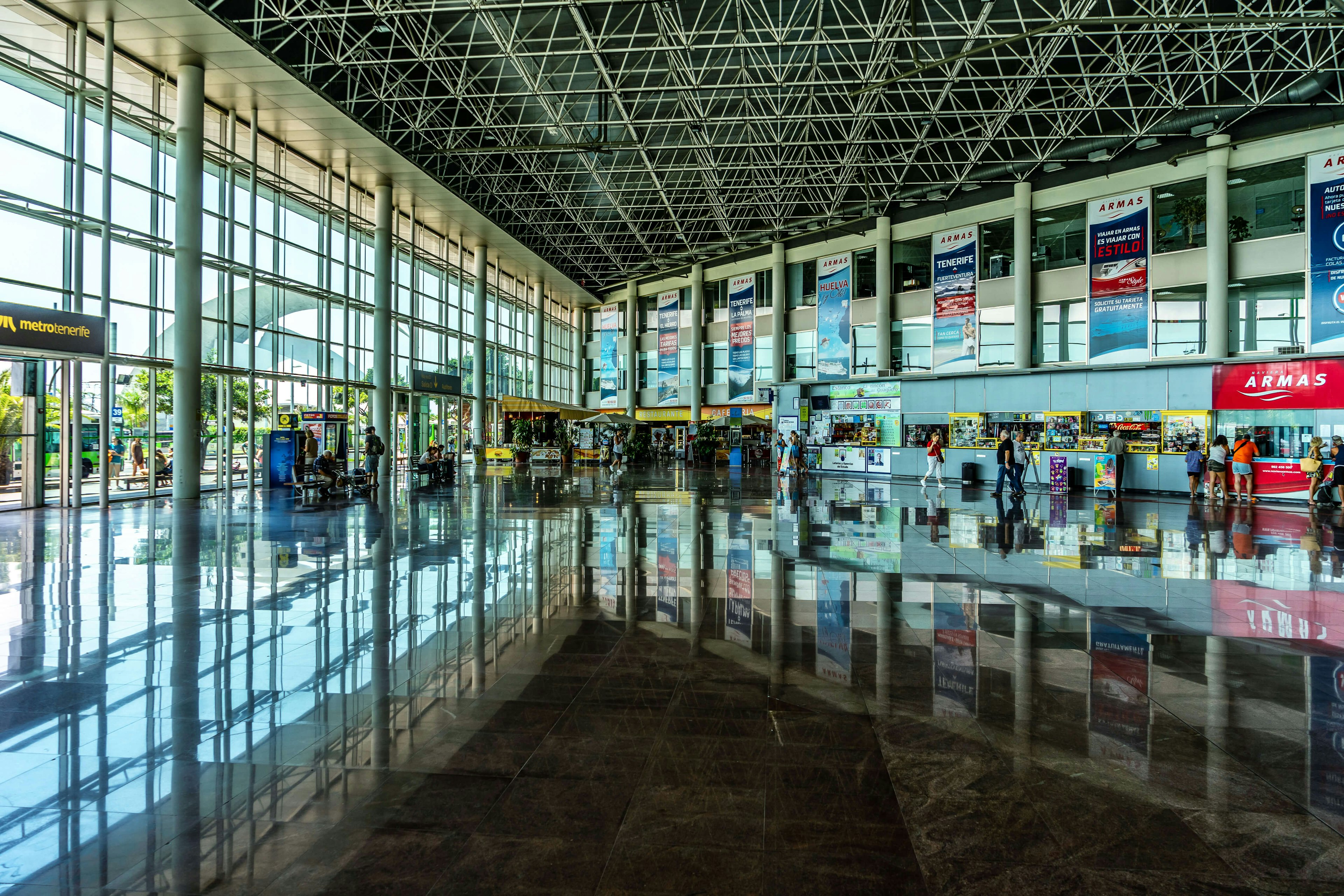 People walking through a bright, modern long-distance bus station with a wall of windows on one side