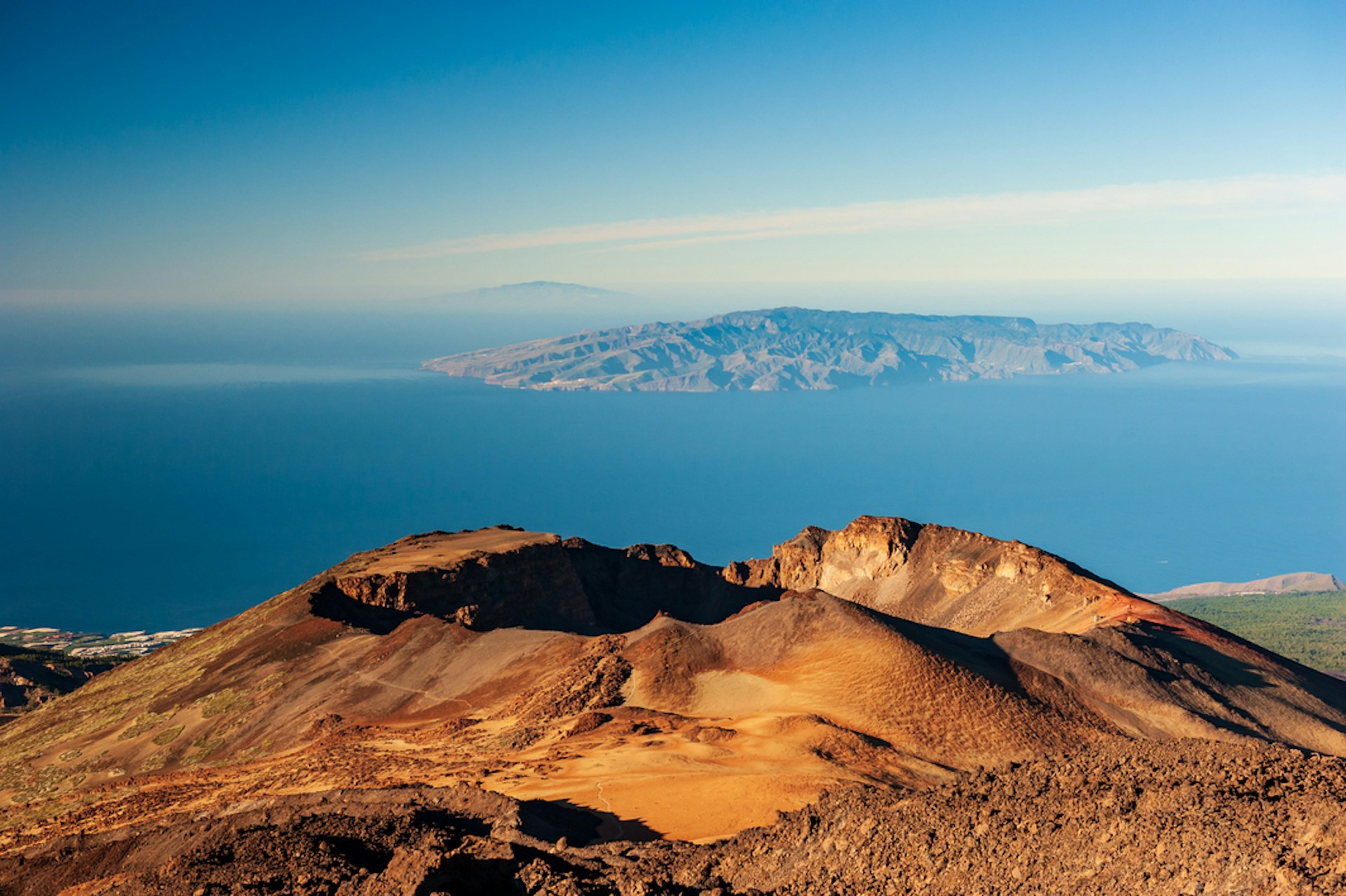 A desert crater at the top of a volcano, with islands out to sea in the distance