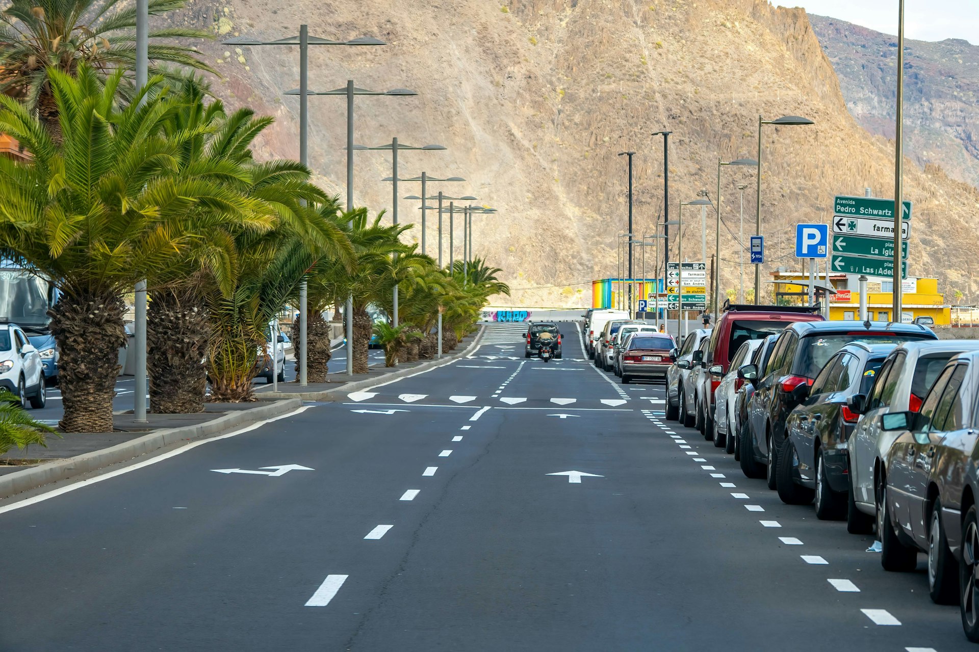 A jeep driving toward a mountain on a road lined with cars