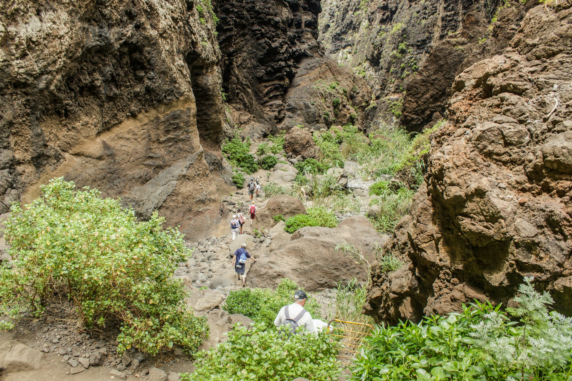 Hikers scramble down a steep path into a gorge with high rock walls