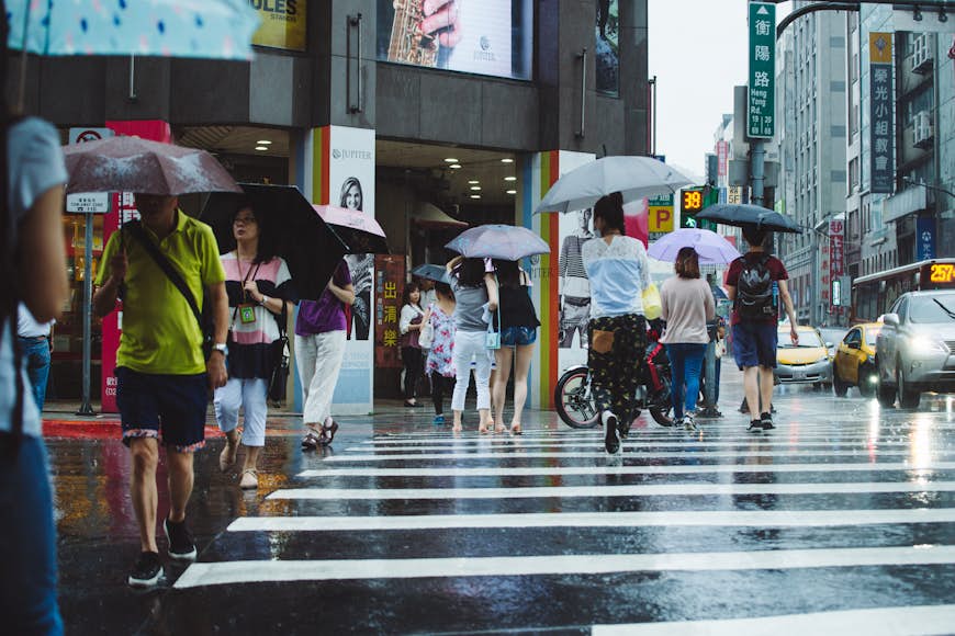 Pedestrians with umbrellas cross a busy street in heavy rain, Taipei, Taiwan