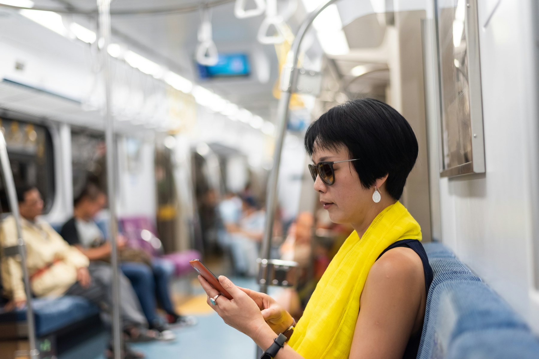 A woman in sunglasses and a yellow scarf looks at her smartphone on the MRT Metro, Taipei, Taiwan