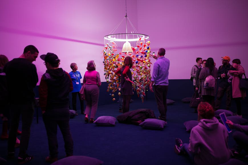 Une pièce où les gens regardent une œuvre d'art qui ressemble à un lustre bas en verre coloré