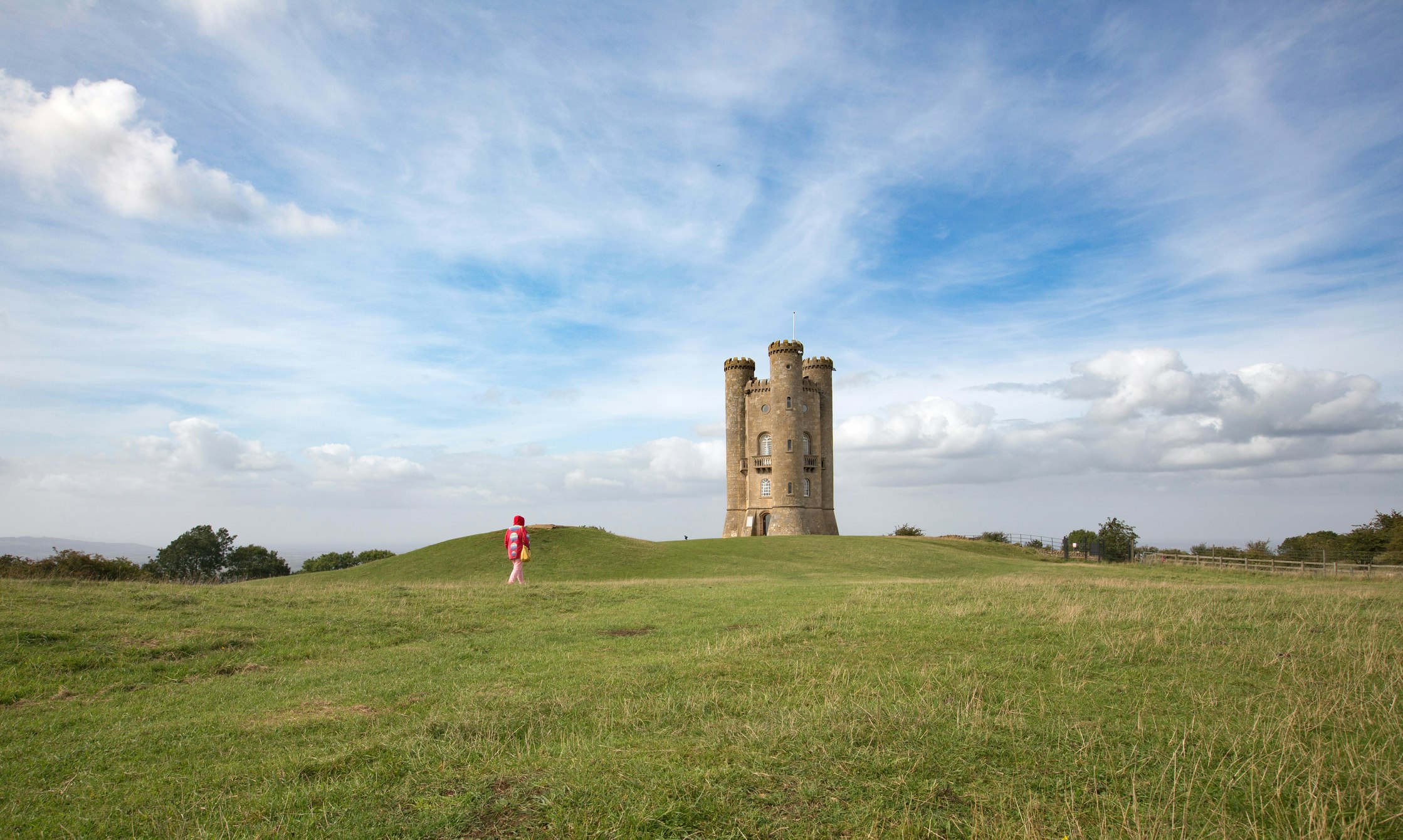 Woman in red walking toward the historic Broadway Tower, Broadway, Worcestershire, the Cotswolds, England, United Kingdom