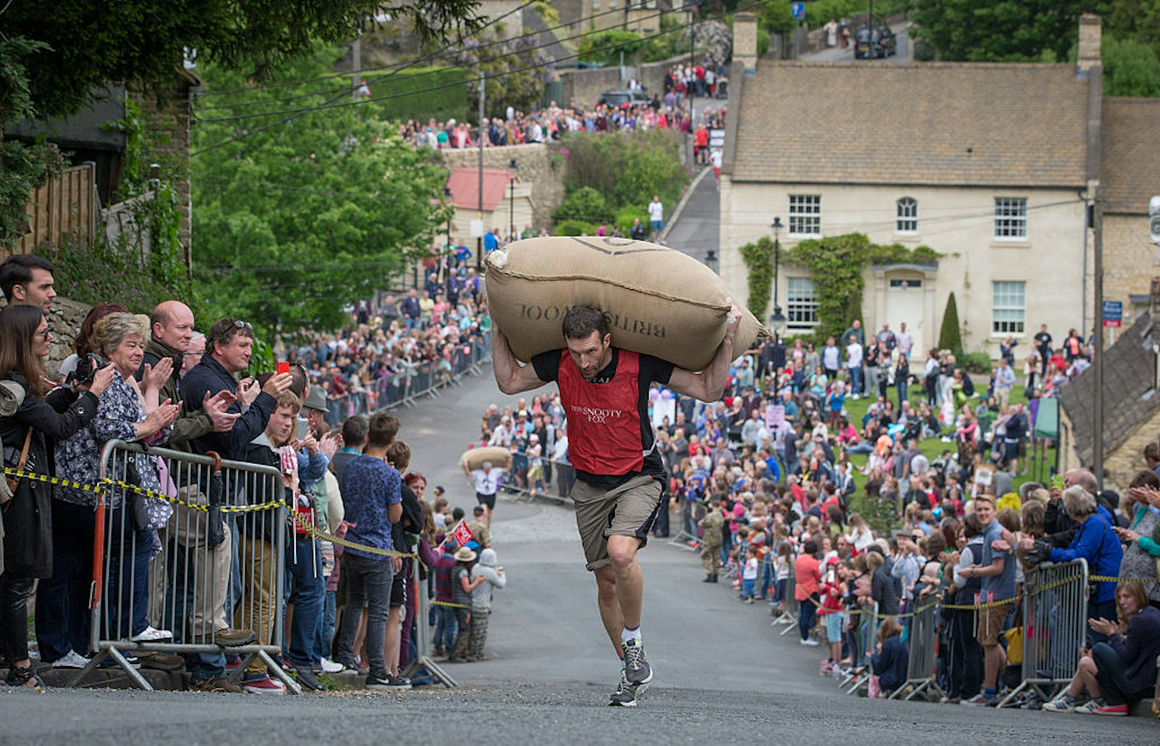 A man races with a sack of wool on his back as spectators watch in the village of Tetbury, Gloucestershire, the Cotswolds, England, United Kingdom