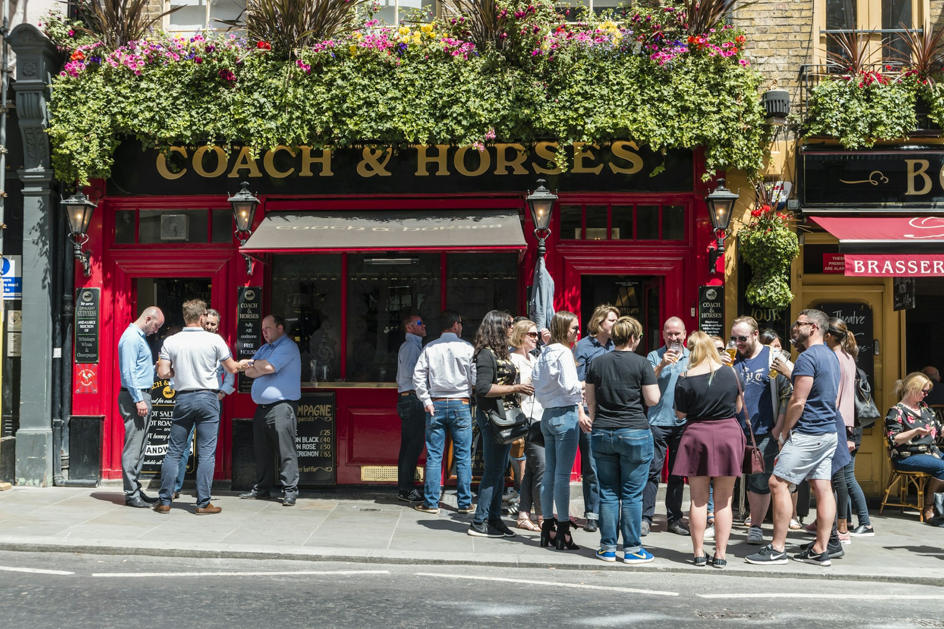 People gather in groups on the sidewalk outside a pub in London enjoying their drinks in the sunshine