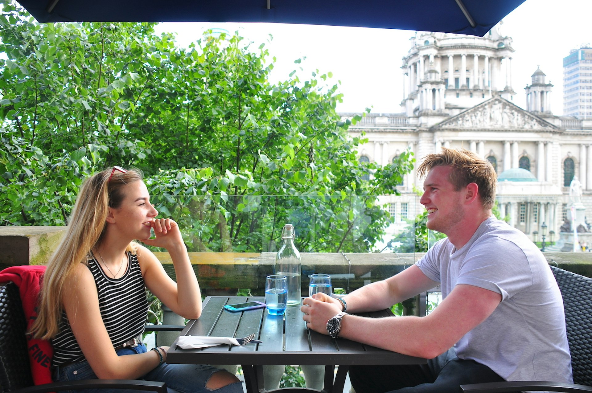 A young couple enjoys a meal at an outdoor table in front of City Hall, Belfast, Northern Ireland, United Kingdom