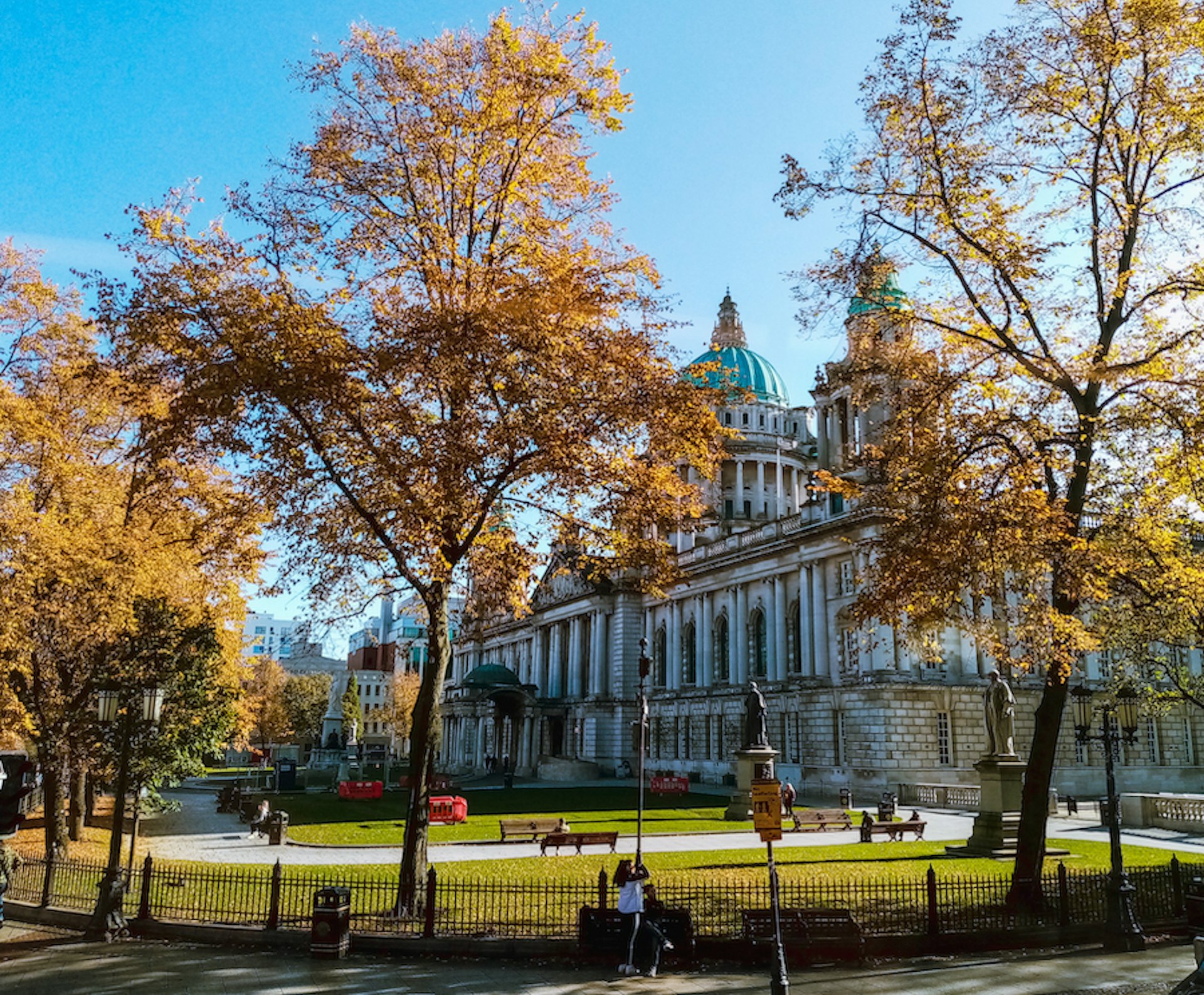 Trees bear gold and brown fall foliage on a sunny day in front of City Hall, Belfast, Northern Ireland, United Kingdom