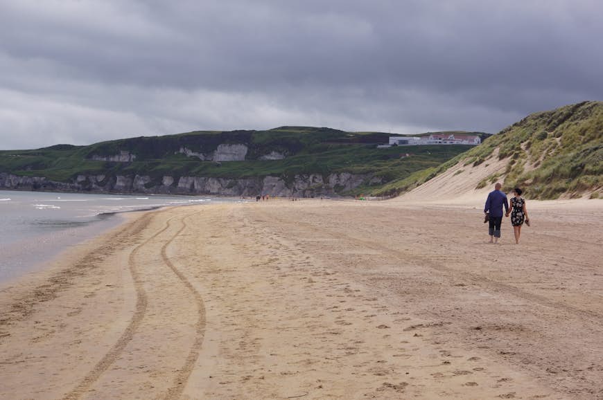 Deux personnes marchent sur la plage de Whiterocks à Portrush, comté d'Antrim, en Irlande du Nord, Royaume-Uni