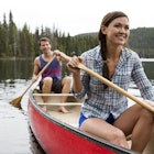 A couple smile while canoeing on a lake.