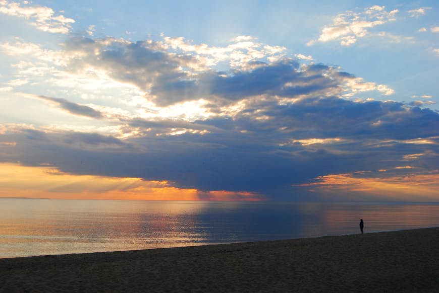 Закат над морем с персонажем в силуэте, стоящим на пляже