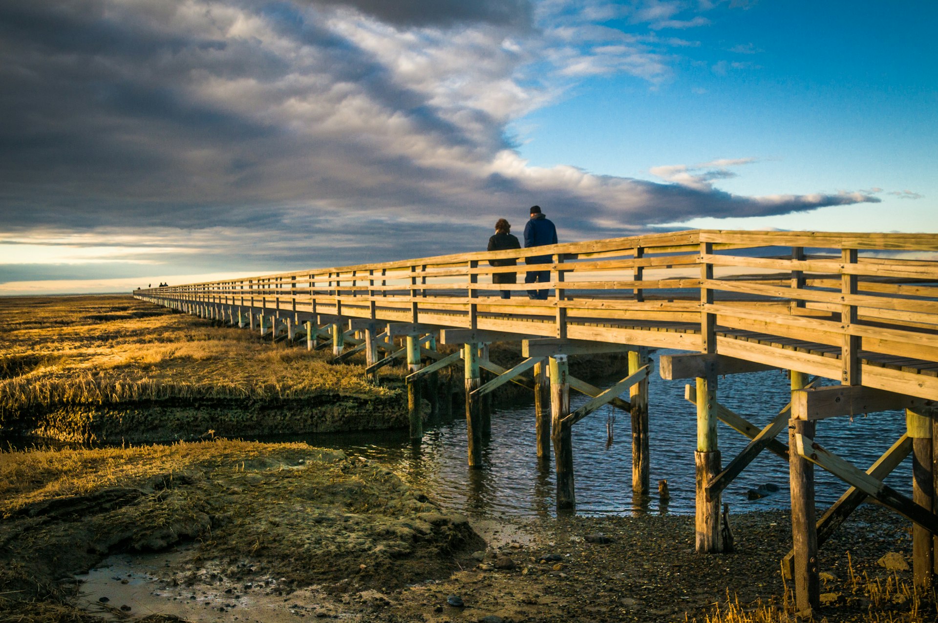 A couple walk along a boardwalk on a winter's day with the sun low in the sky