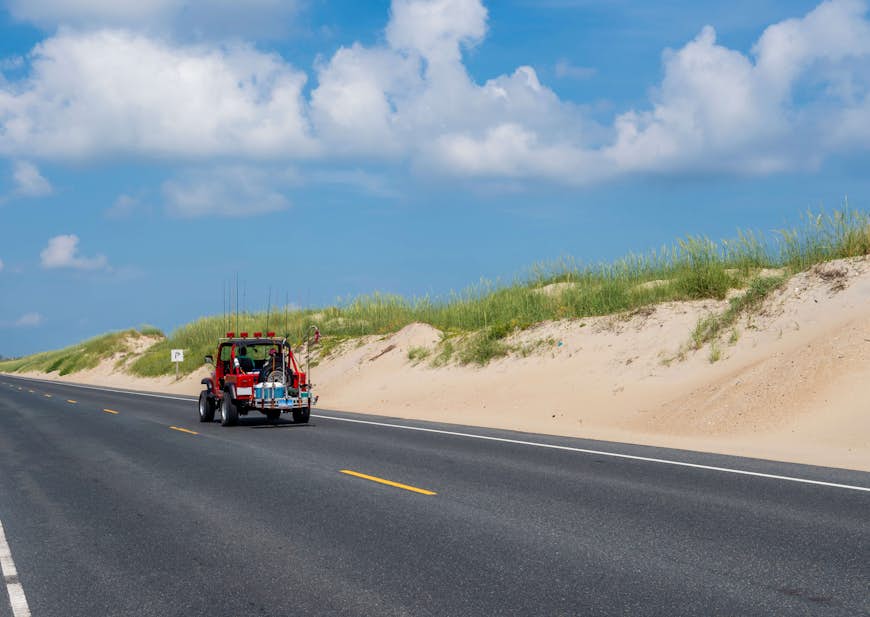 A jeep drives down highway 12 on the Outer Banks, with dunes on one side