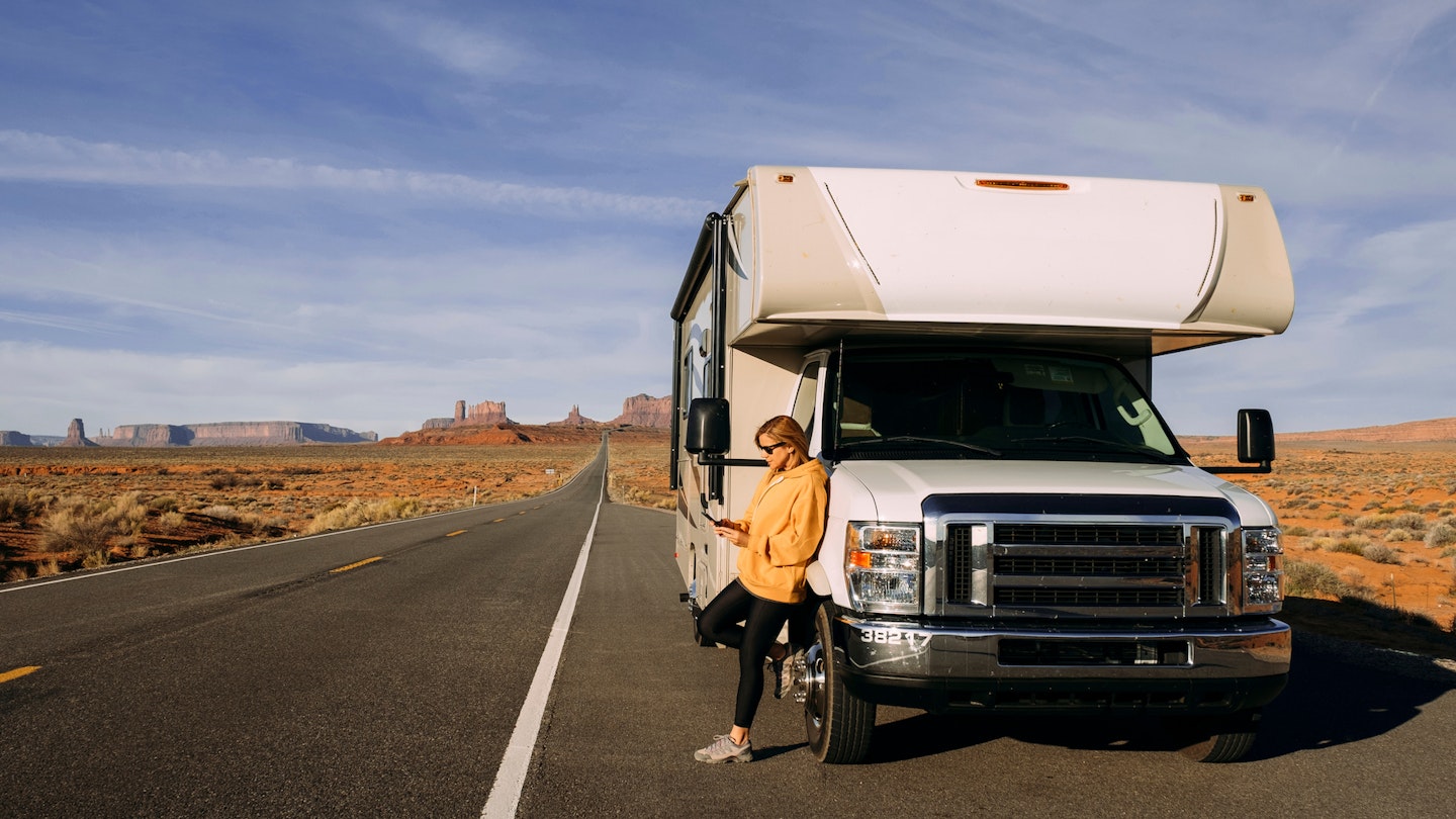A woman travels by motorhome through Monument Valley in the USA desert and checks her mobile phone parked on the side of the road; Shutterstock ID 1664258755; your: Brian Healy; gl: 65050; netsuite: Lonely Planet Online Editorial; full: Best road trips in Utah