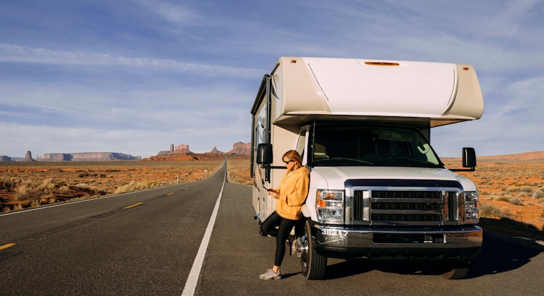 A woman travels by motorhome through Monument Valley in the USA desert and checks her mobile phone parked on the side of the road; Shutterstock ID 1664258755; your: Brian Healy; gl: 65050; netsuite: Lonely Planet Online Editorial; full: Best road trips in Utah