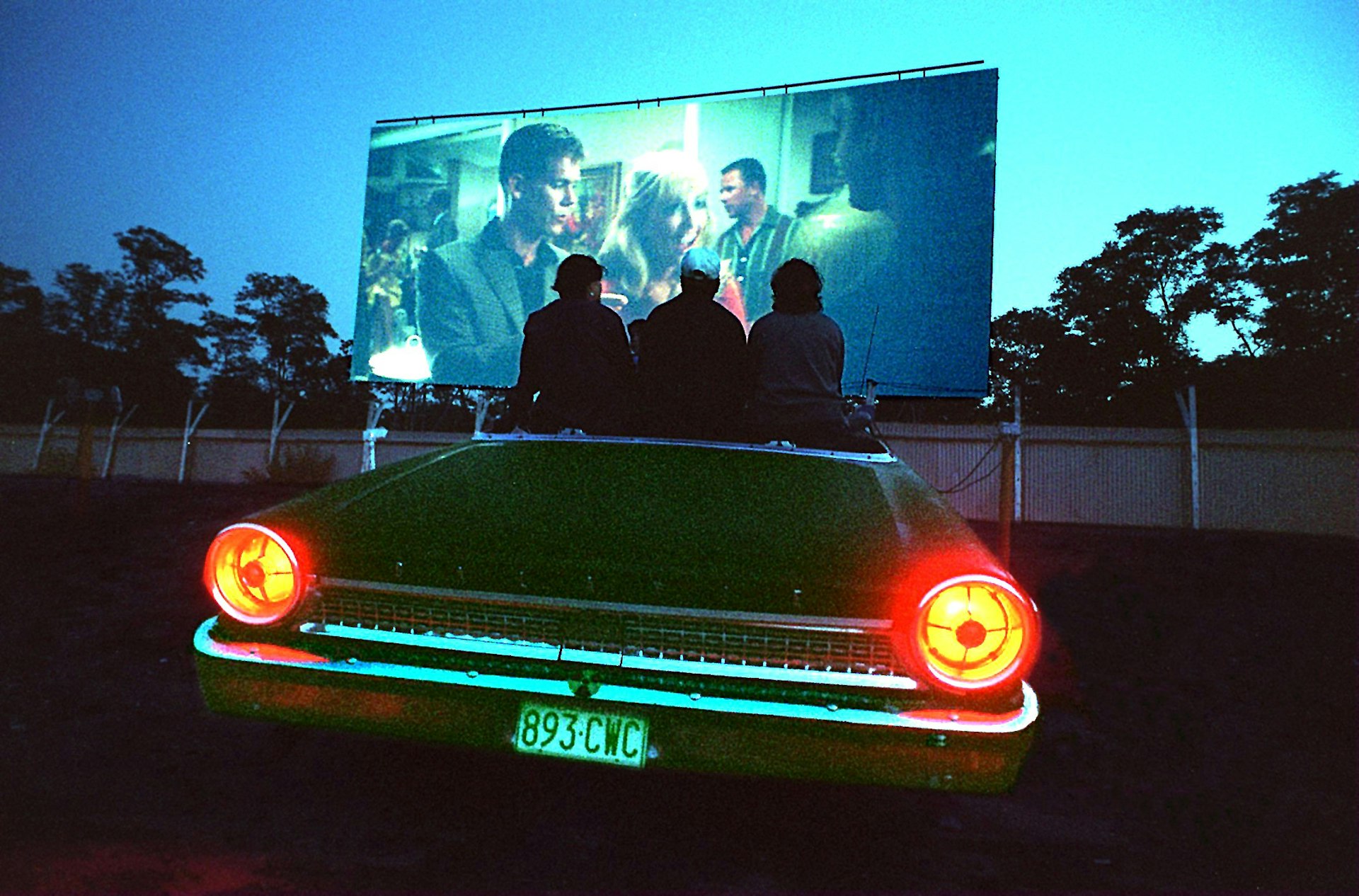 A trop of people sit on the edge of a top-down car watching a movie at the Wellfleet Drive-In in Cape Cod, Massachusetts.