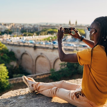 A view from the back of a Brazilian man taking a photo with his mobile phone of a view from the top of the fortress