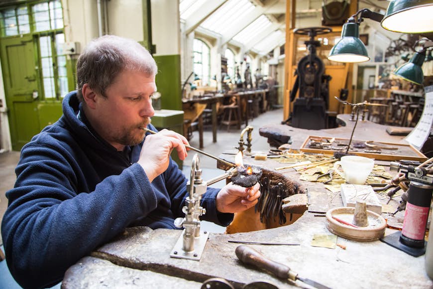 A jewelry-maker works with a flame on a metal piece of jewlry in a workshop