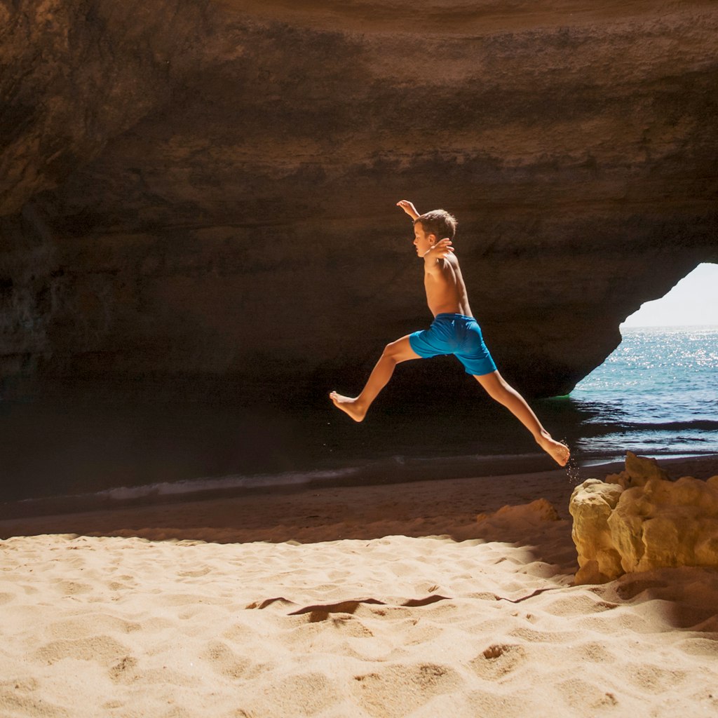 Little boy jumping from cliff in famous Benagil cave on the coast of the Algarve in Portugal.