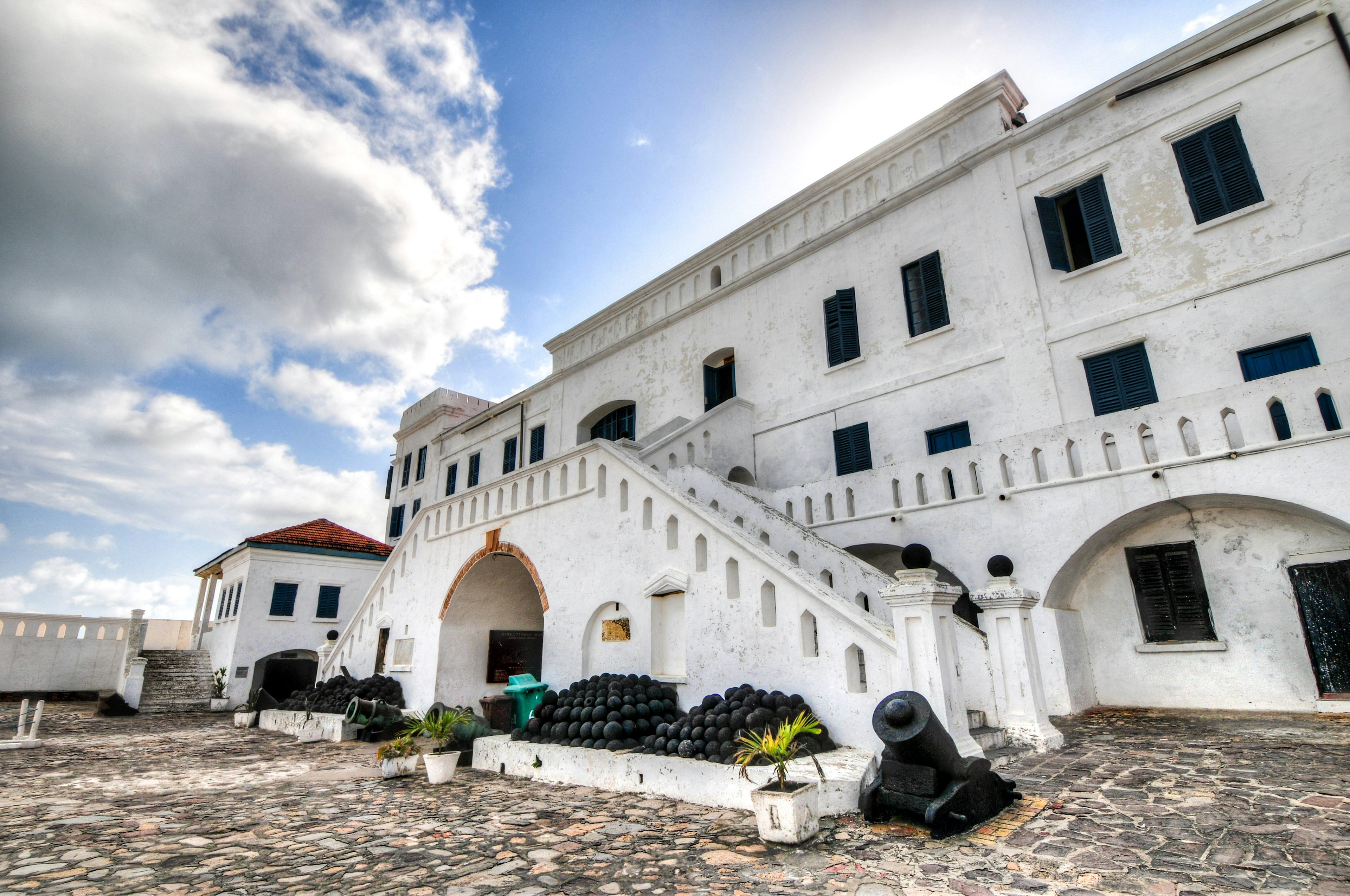 The whitewashed facade of Cape Coast Castle under a bright blue sky with sparse clouds