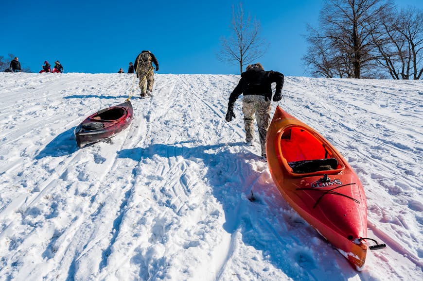 Two men drag their kayaks up a park hill after sledding down
