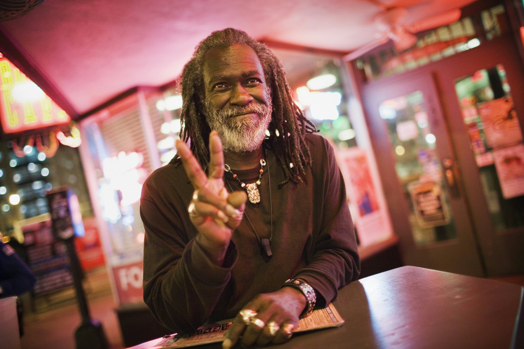 A man smiles at the camera and gives a two-finger peace sign