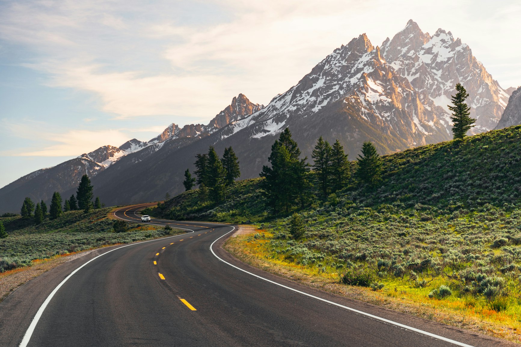 A winding road leads to the Teton Mountain Range at sunset in Grand Teton National Park, Wyoming.

