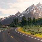 A winding road leads to the Teton Mountain Range at sunset in Grand Teton National Park, Wyoming.


