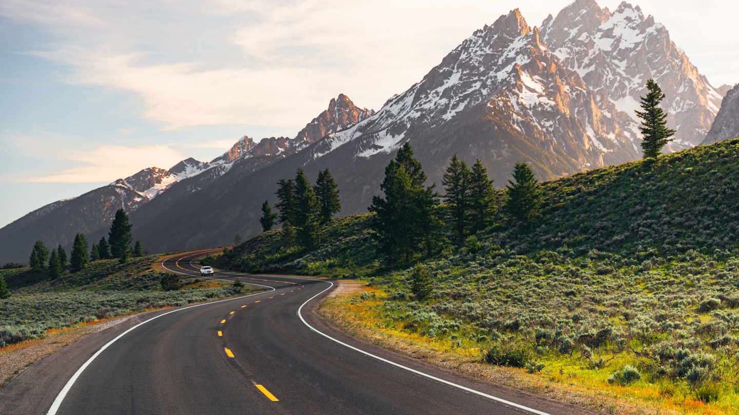 A winding road leads to the Teton Mountain Range at sunset in Grand Teton National Park, Wyoming.
