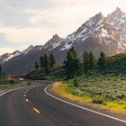 A winding road leads to the Teton Mountain Range at sunset in Grand Teton National Park, Wyoming.