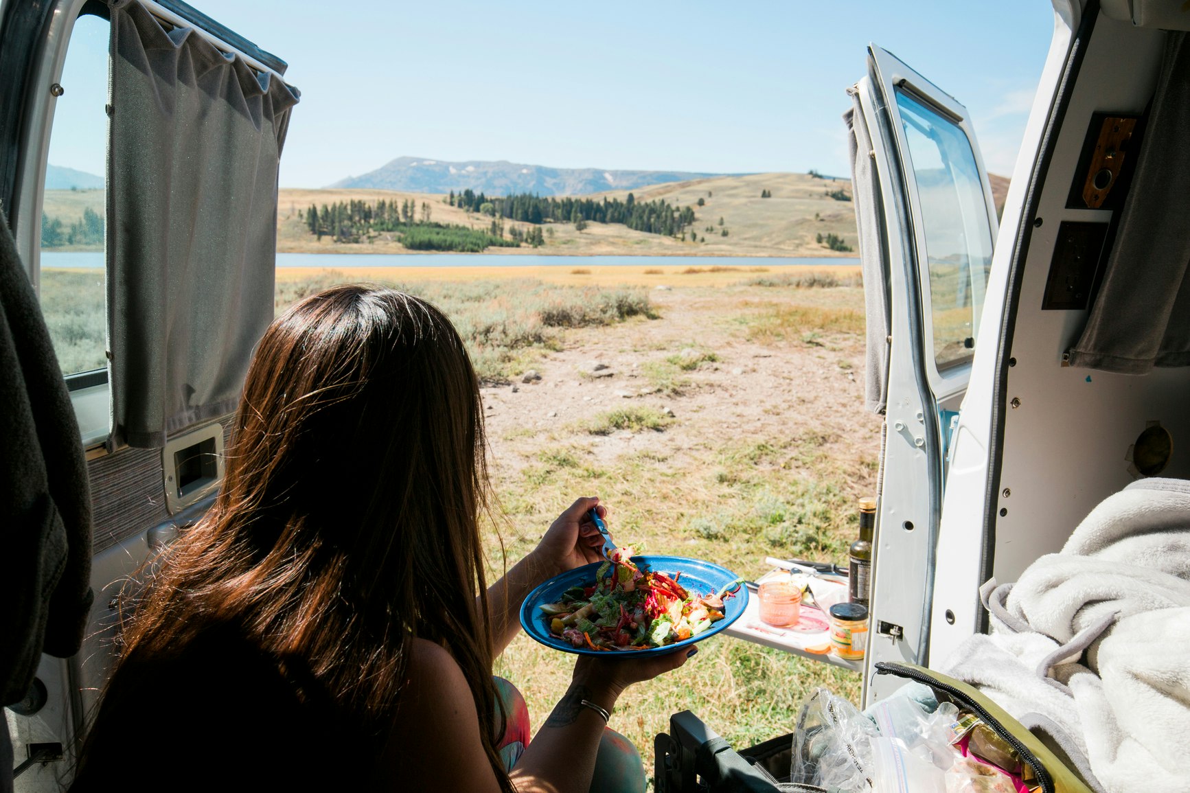 Woman inside a van eating from a plate while looking out to the Yellowstone landscape
