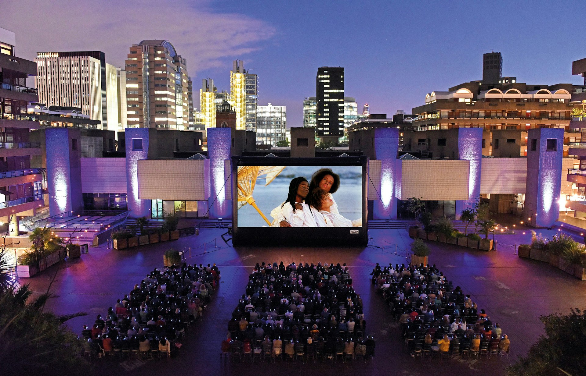 People watching a movie on a big screen at dusk at the Barbican Outdoor Cinema