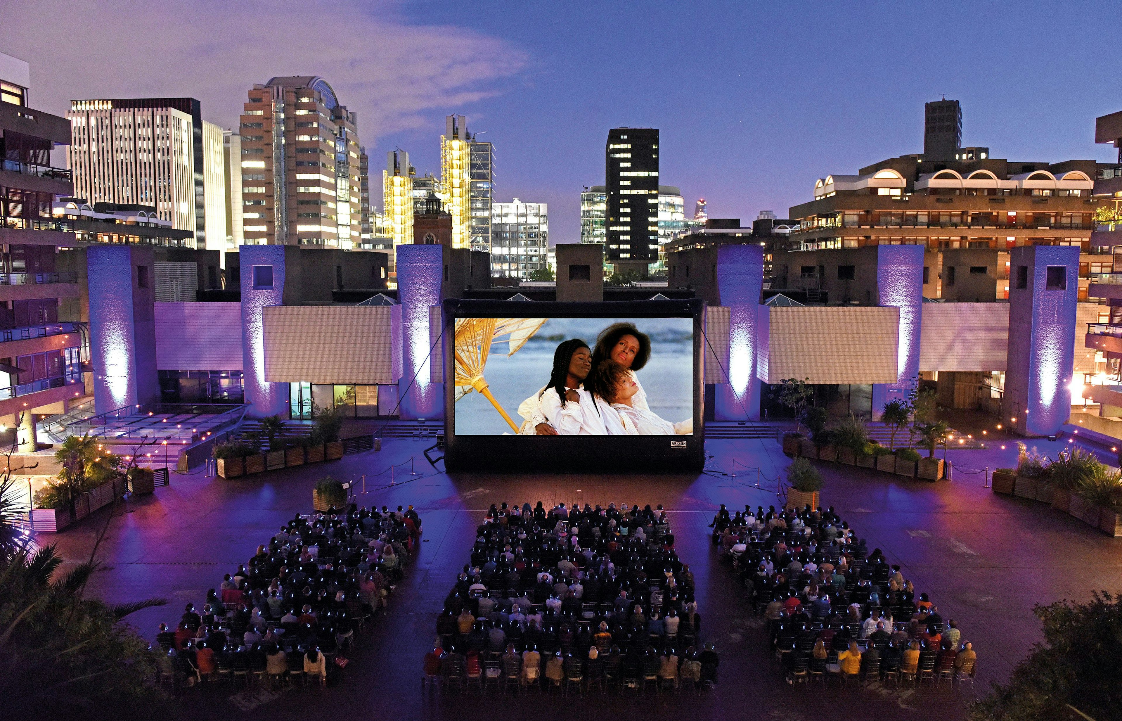 People watching a movie on a big screen at dusk at the Barbican Outdoor Cinema