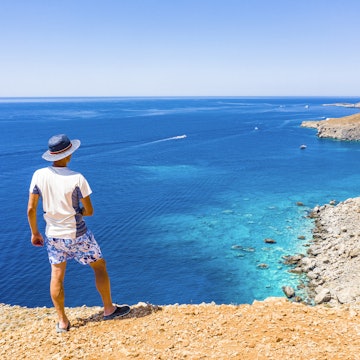 Tourist with sun hat looking down at the sea from cliffs near Hora Sfakion, Crete