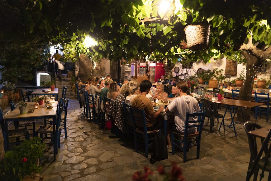 Group of friends sitting around table enjoying al fresco dining at a taverna in Crete