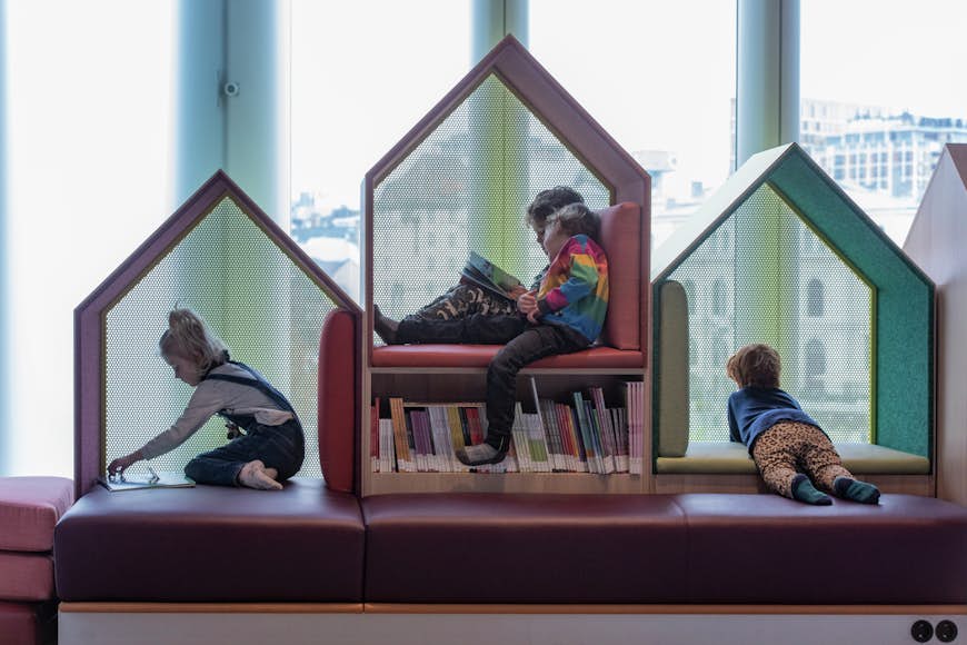 Three young children read books in the children's scetion of the Deichman Library, Oslo inside some small geometric-style houses