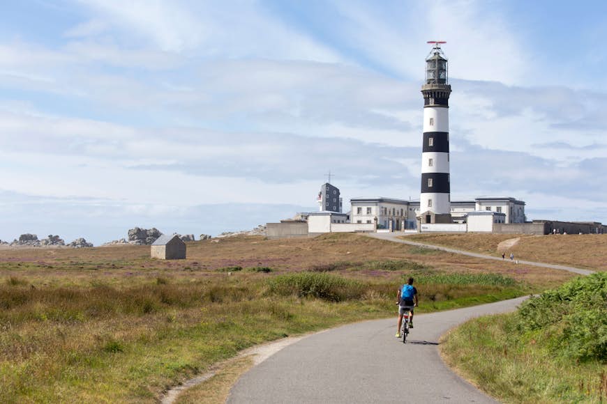 Person cycling past a lighthouse on lighthouse on Île d’Ouessant, France
