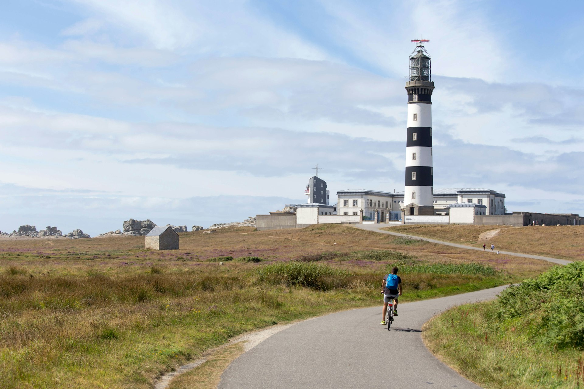 Person cycling past a lighthouse on lighthouse on Île d’Ouessant, France