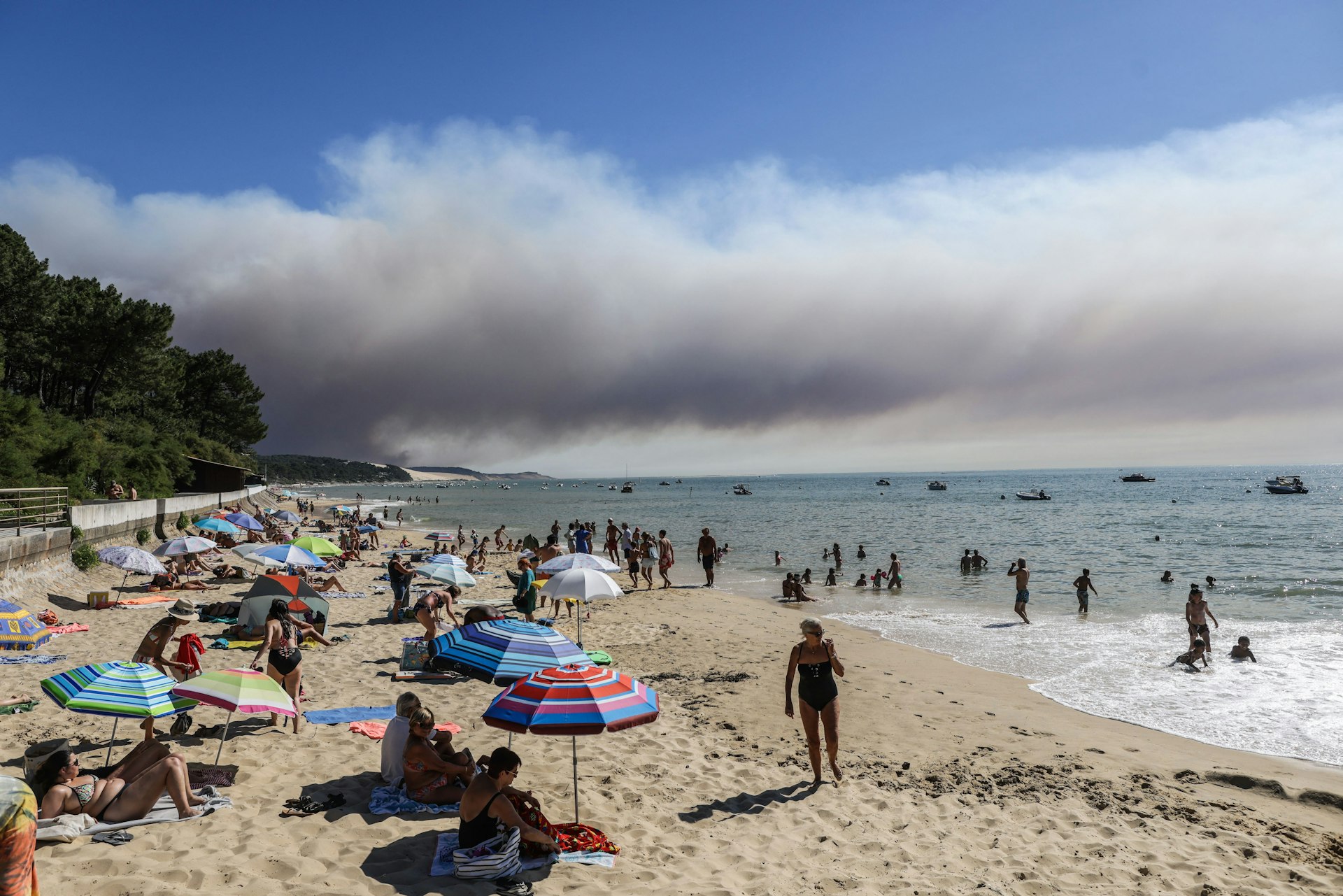 Beach-goers bathe and lay at a beach of "Pyla sur mer" as a black cloud of smoke from a fire that hit La Teste-de-Buch forest rises 